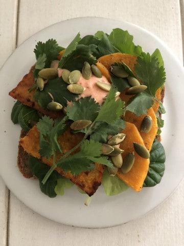 Open sandwich topped with lettuce, roasted squash, creamy sauce and pepitas on a plate