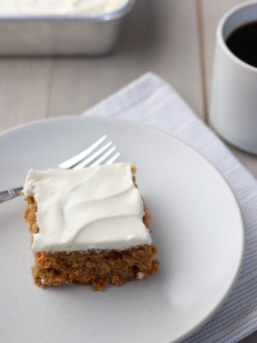 A piece of carrot cake on a plate with a fork, napkin and cup of coffee