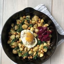 A skillet filled with pytt i panna, a fried egg and pickled beets on a kitchen towel