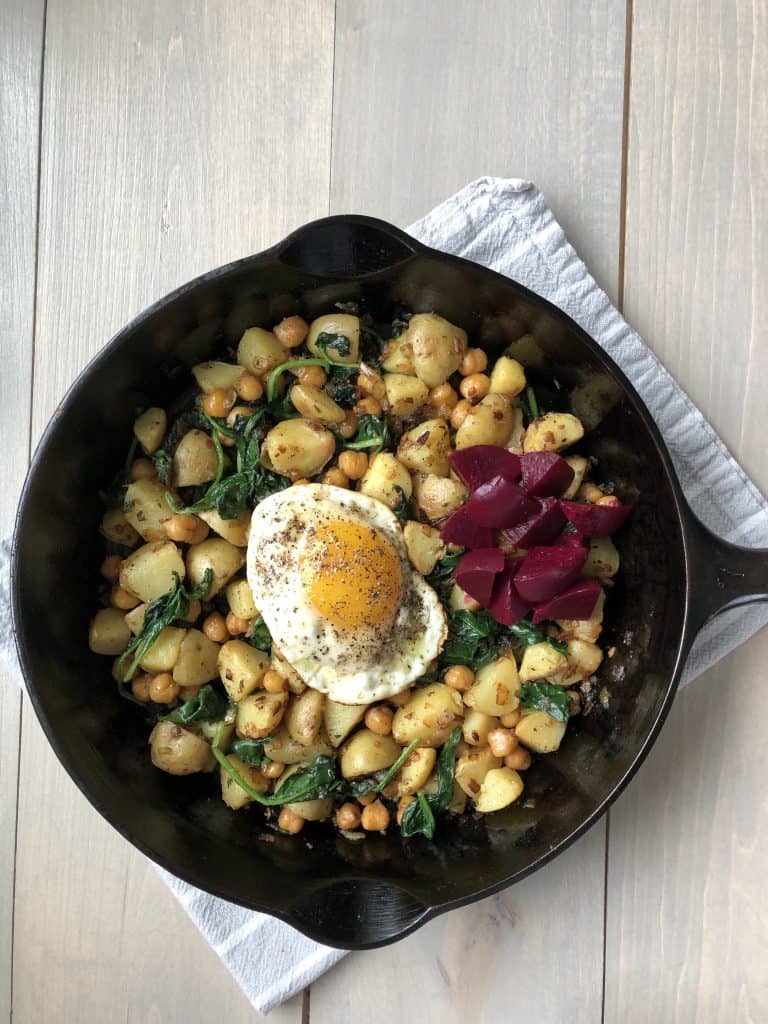 A skillet filled with pytt i panna, a fried egg and pickled beets on a kitchen towel