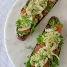 Open sandwiches topped with lettuce, salmon and fennel on a marble plate