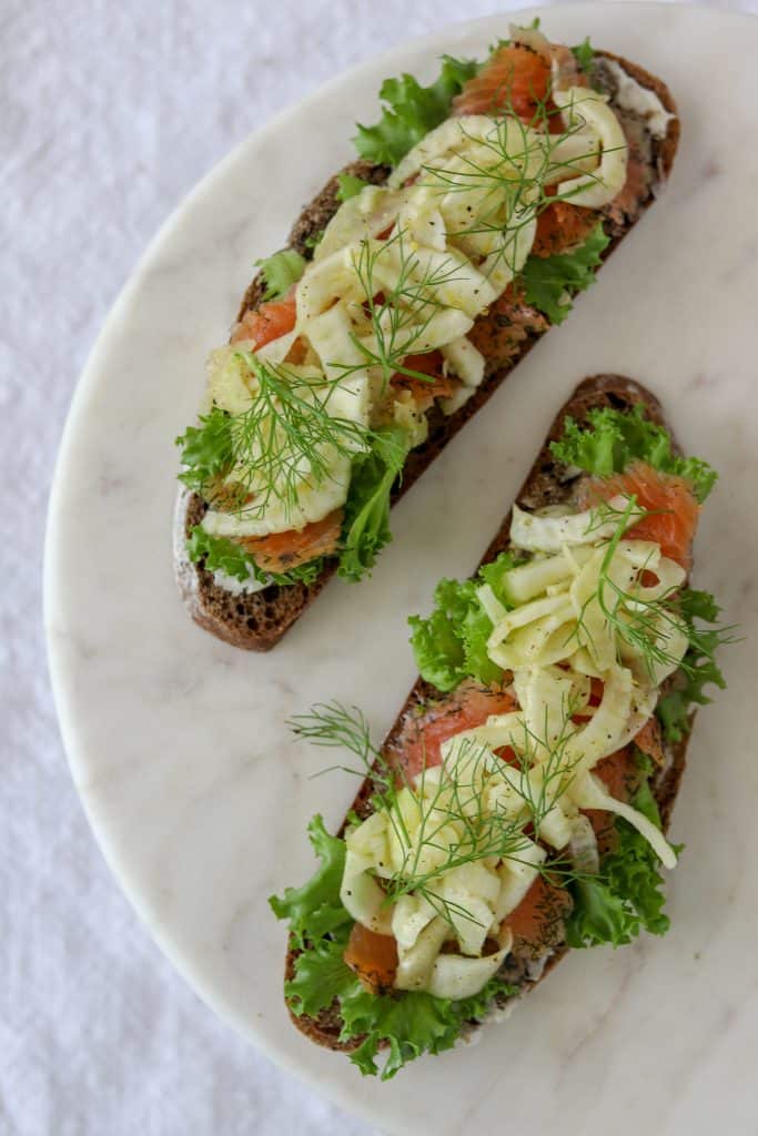 Open sandwiches topped with lettuce, salmon and fennel on a marble plate