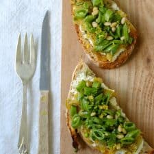 Open sandwiches topped with snap peas and leeks on a wooden cutting board next to a knife and fork