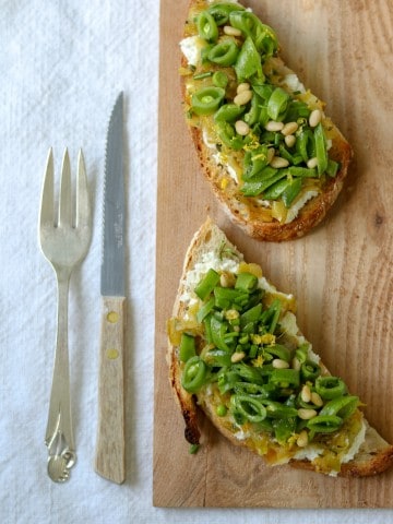 Open sandwiches topped with snap peas and leeks on a wooden cutting board next to a knife and fork