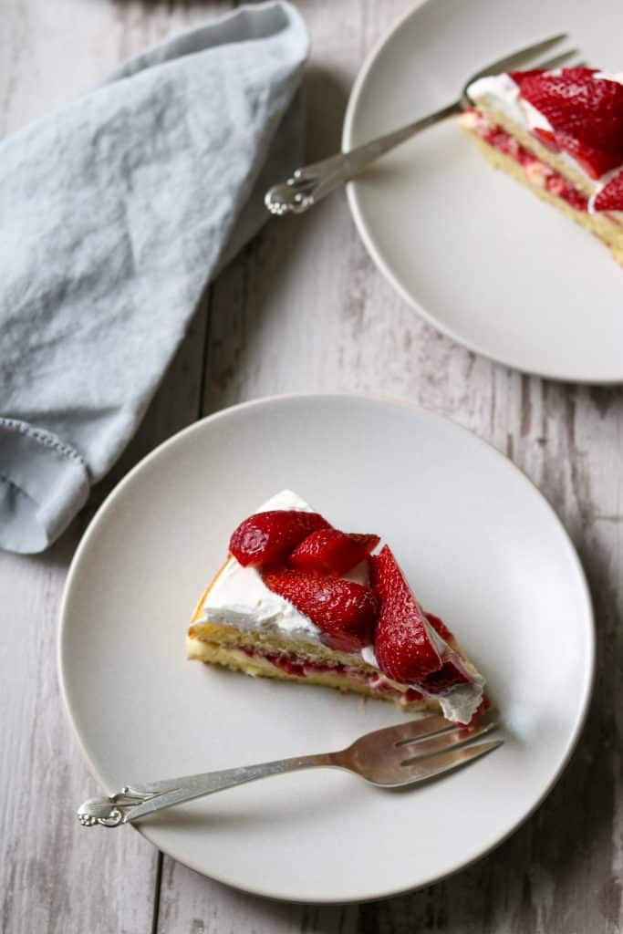 A slice of strawberry cream cake on a plate with a fork and napkin