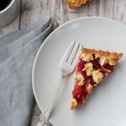 A slice of strawberry almond tart on a plate with a fork, napkin and cup of coffee