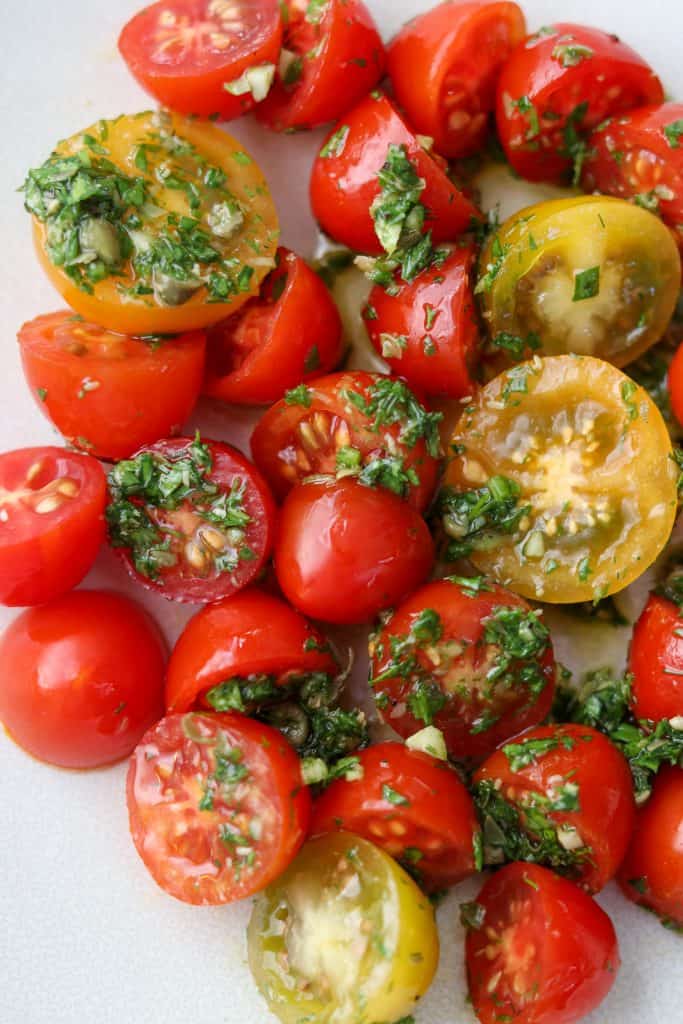 A close up of cherry tomatoes tossed with fresh herb sauce