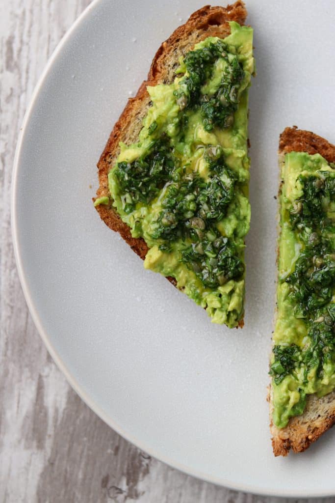 Toast topped with mashed avocado and fresh herb sauce on a plate