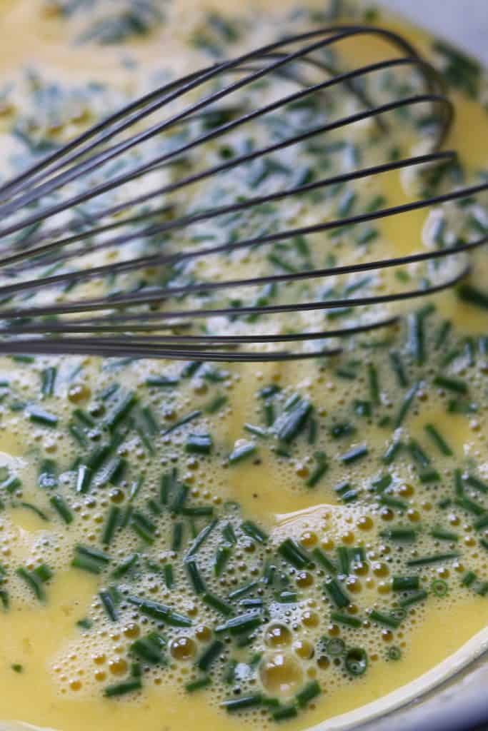 A close up of beaten eggs and chives with a whisk