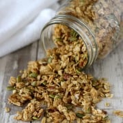 Granola spilling from a jar onto a wooden surface next to a towel