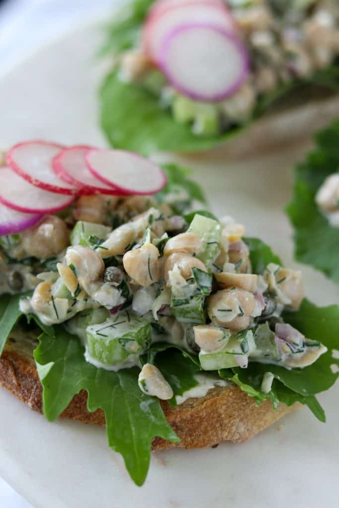 A close up of an open face sandwich topped with lettuce, chickpea salad and radishes