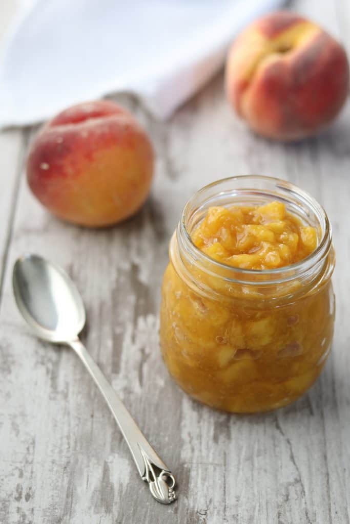 Roasted peach ginger compote in a jar next to a spoon and fresh peaches