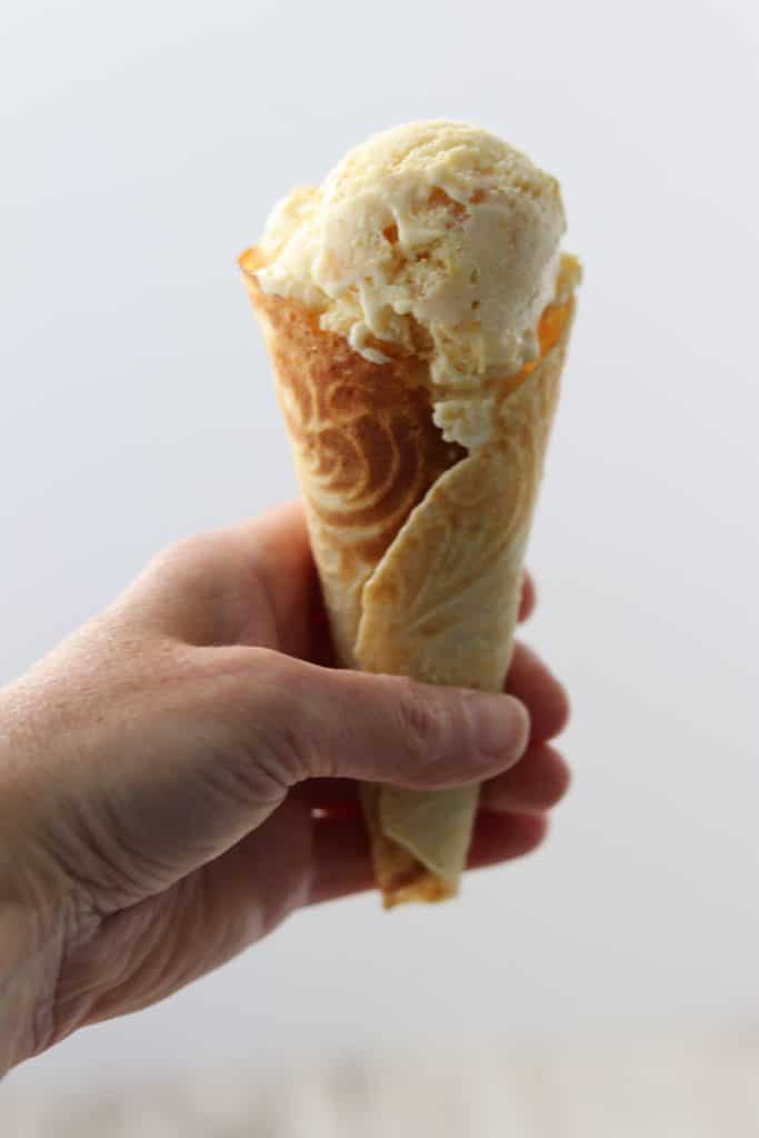 A hand holding an ice cream cone filled with peach ice cream