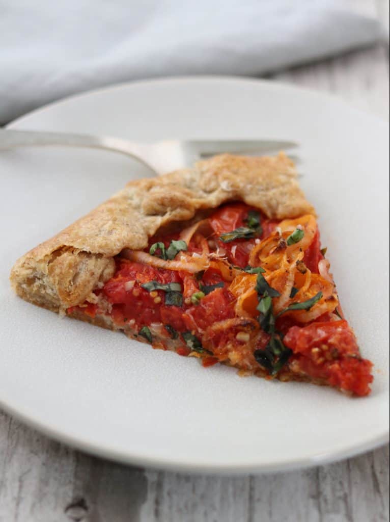 A slice of tomato tart on a plate with a fork