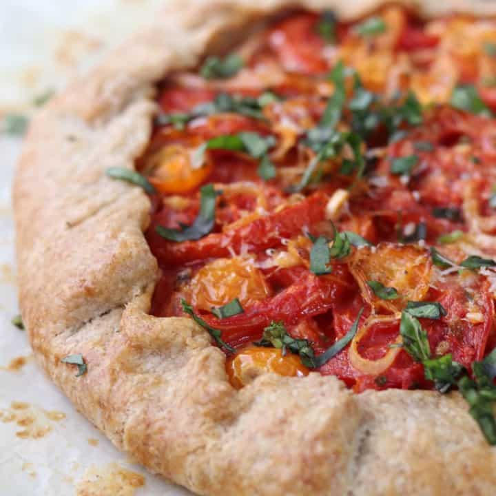 A close up of a rustic tomato tart topped with basil
