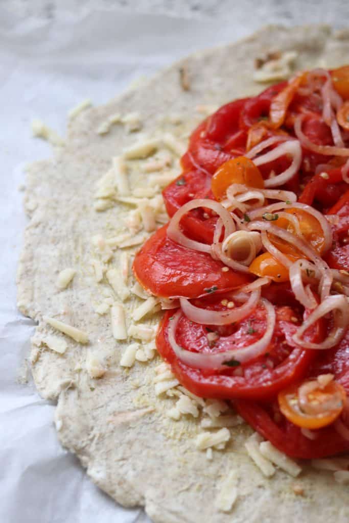 Tart dough topped with cheese, sliced tomatoes and shallots