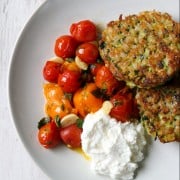 Zucchini barley cakes, roasted cherry tomatoes and ricotta cheese on a a plate