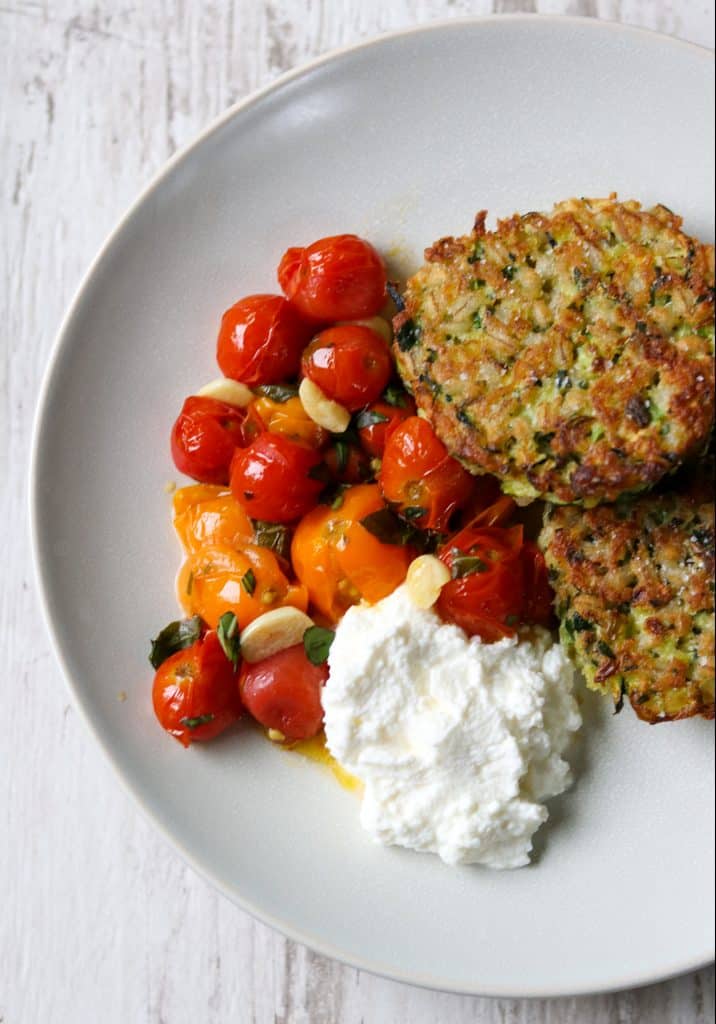 Zucchini barley cakes, roasted cherry tomatoes and ricotta cheese on a a plate