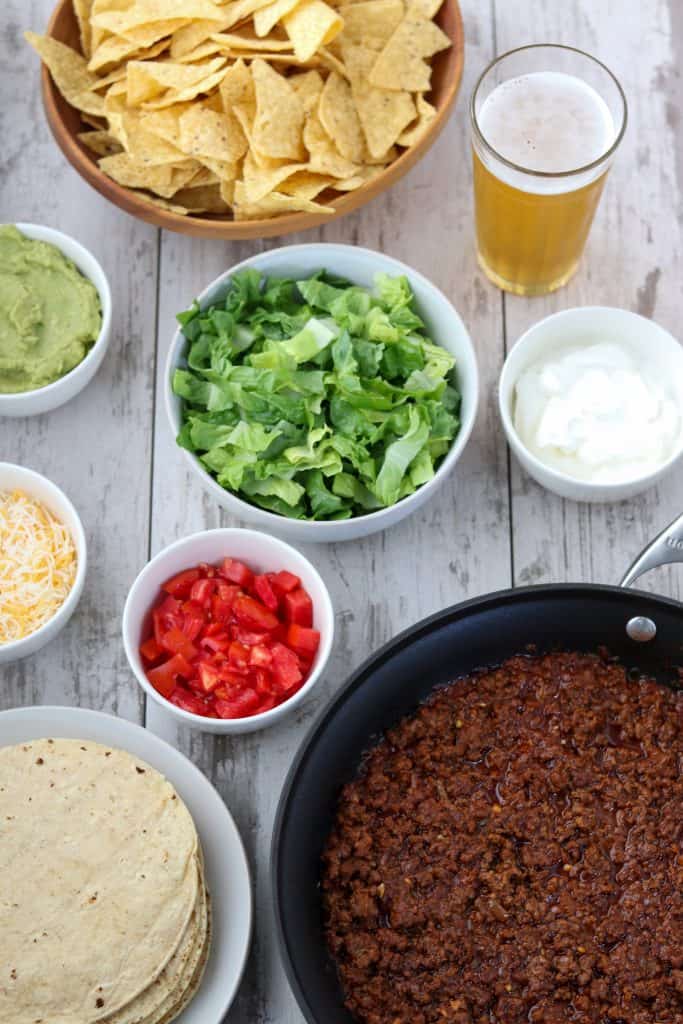 Taco ingredients in bowls with a beer on a wooden surface