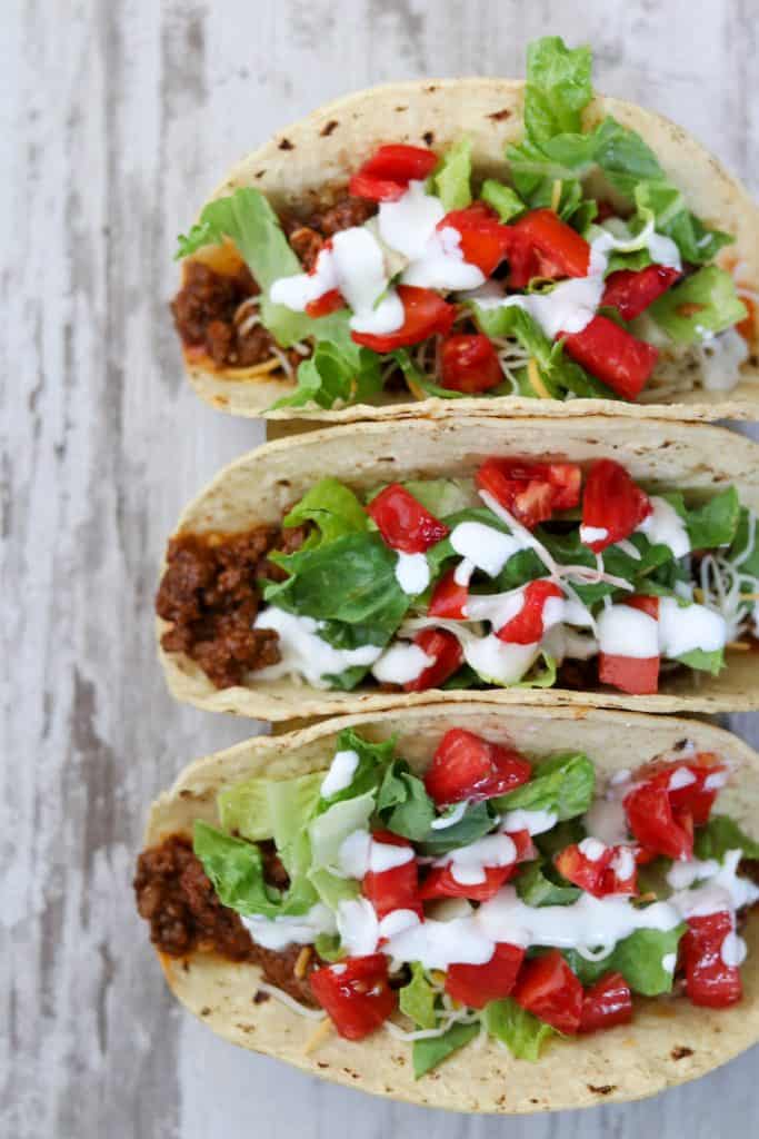 Three tacos with toppings on a wooden surface