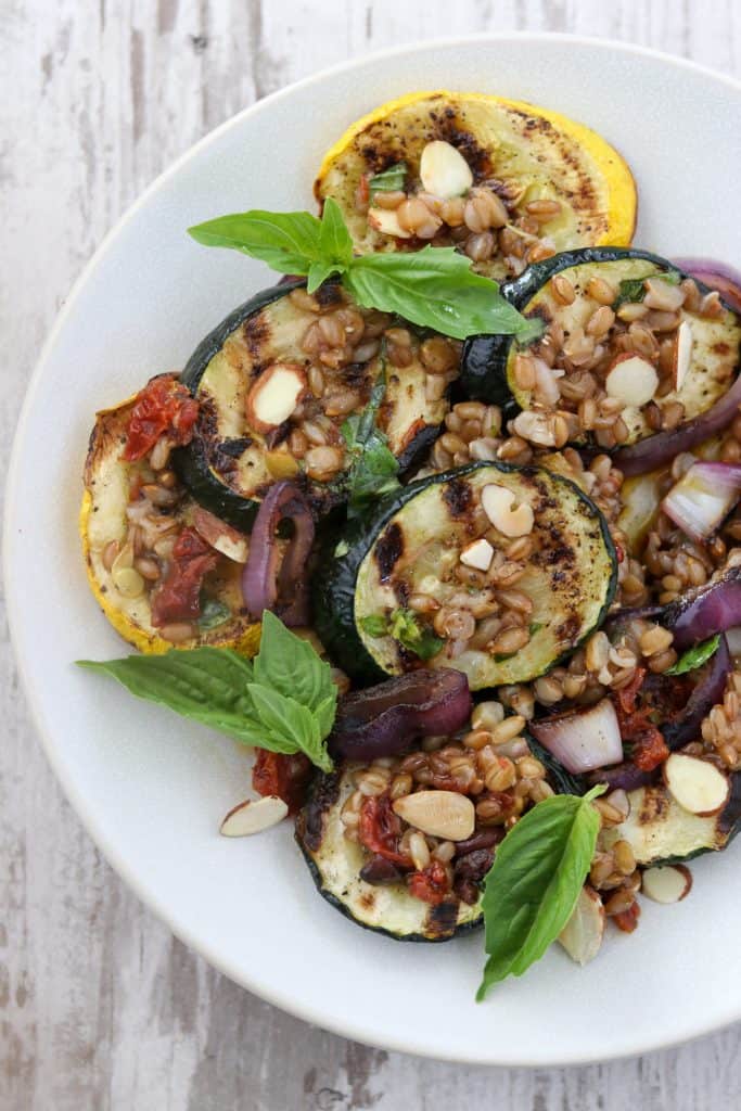 A plate of grilled summer squash salad topped with basil leaves