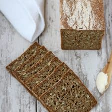 Slices of rye bread and a wooden knife with butter on a wooden surface