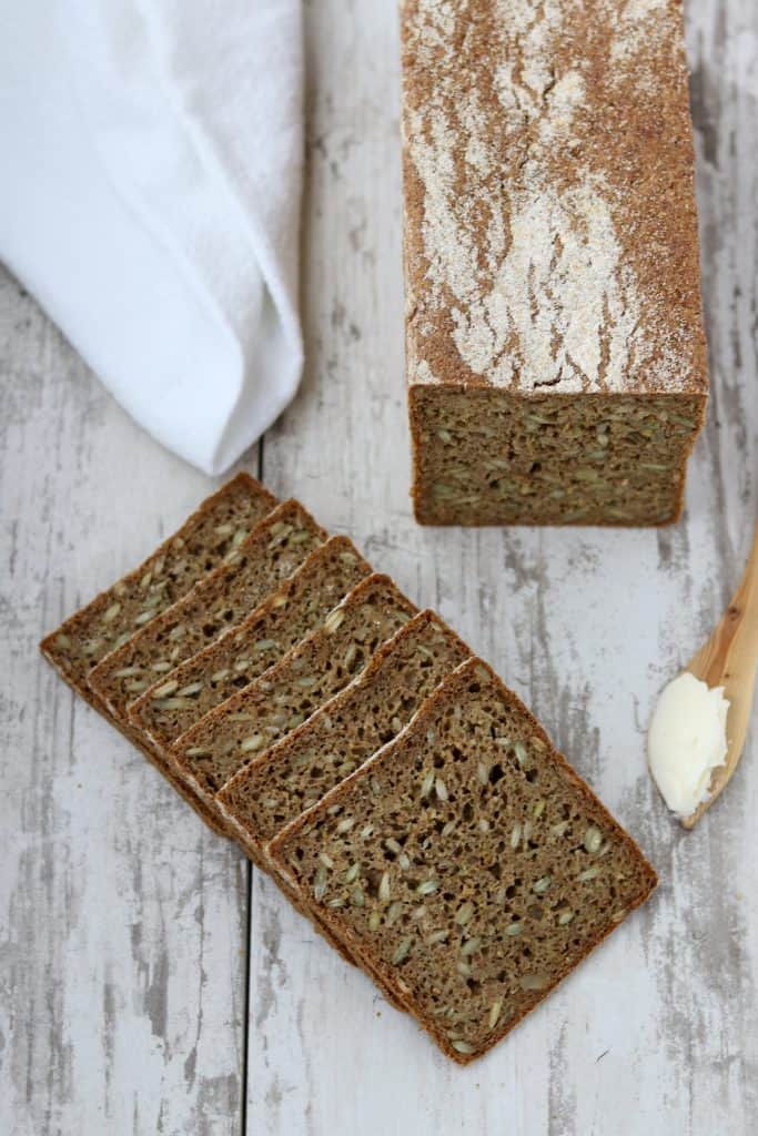 Slices of rye bread and a wooden knife with butter on a wooden surface