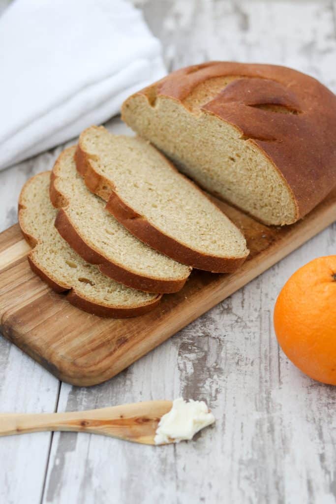 Sliced limpa bread on top of a wooden cutting board next to an orange