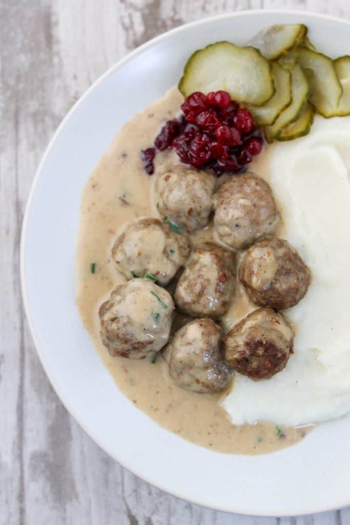 Swedish meatballs in gravy with mashed potatoes, lingonberries and pickles on a plate