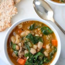 A bowl of white bean and sausage soup with Swiss chard with a spoon and crispbread