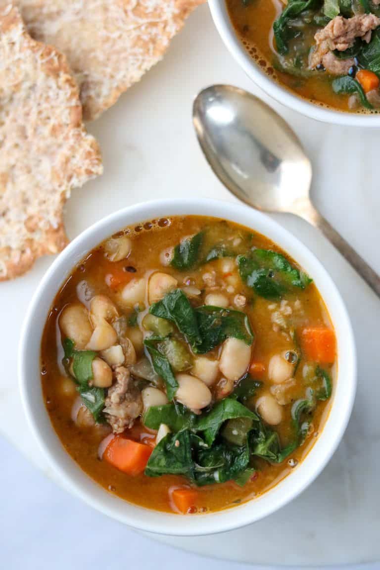 A bowl of white bean and sausage soup with Swiss chard with a spoon and crispbread