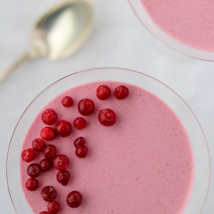 Lingonberry mousse topped with lingonberries in a glass next to a spoon