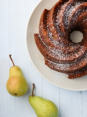 A pear cardamom bundt cake on a plate with two pears