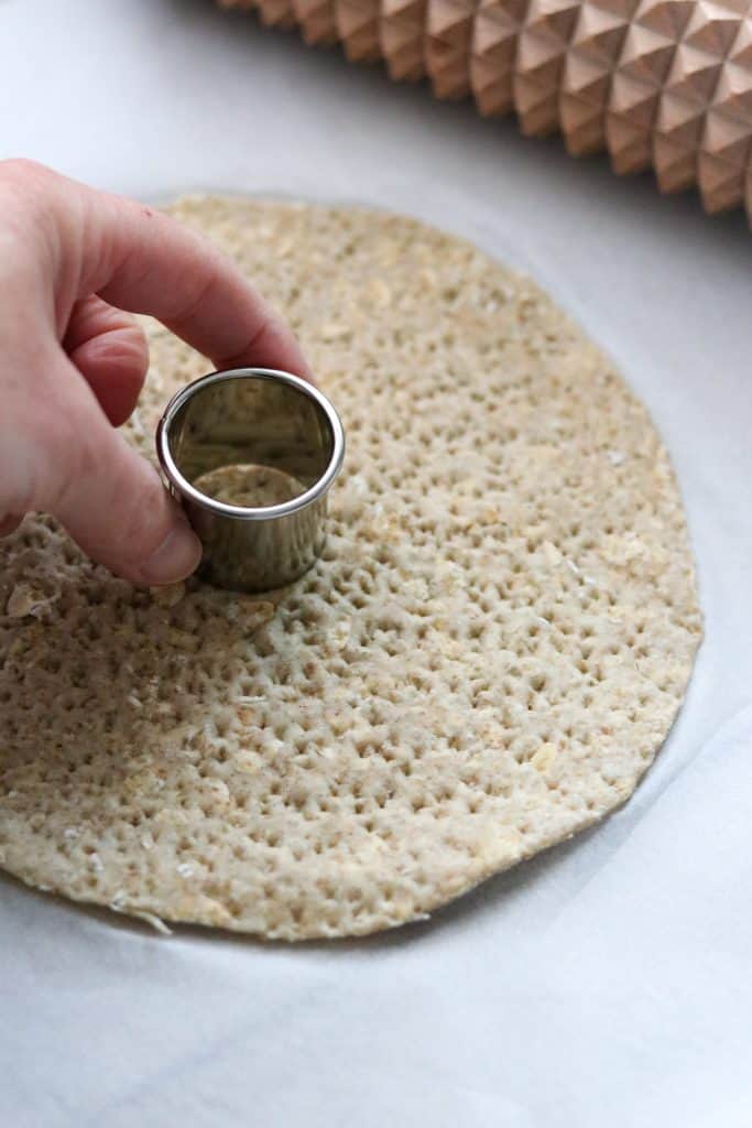 A person cutting a hole out of a piece of Swedish crispbread