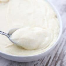 A bowl of potato and celery root puree with a spoon on a wooden surface