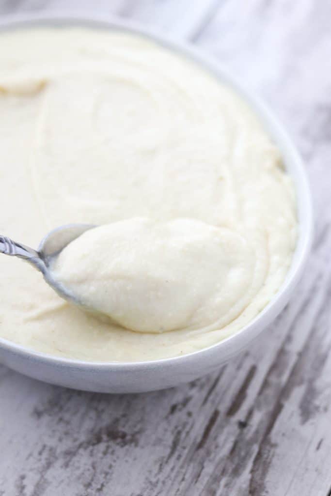 A bowl of potato and celery root puree with a spoon on a wooden surface