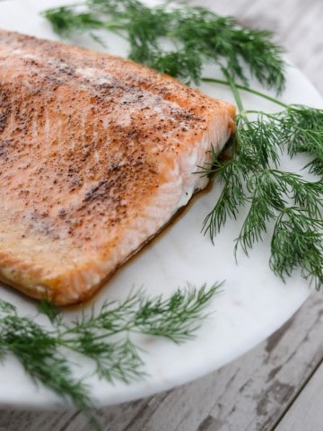 A piece of salmon on a plate with fresh dill