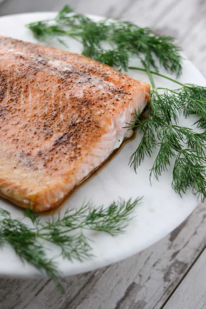 A piece of salmon on a plate with fresh dill