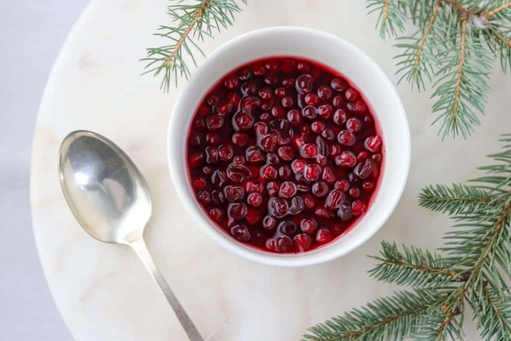 Bowl of lingonberries with a spoon and evergreen branches