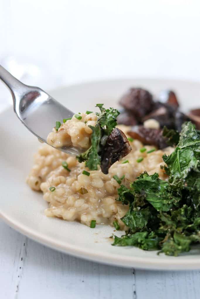 A close up of a bite of barley risotto, mushroom and kale on a fork