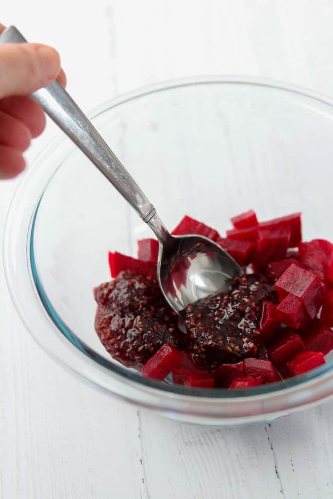 A bowl of roasted beets and raspberry jam with a spoon