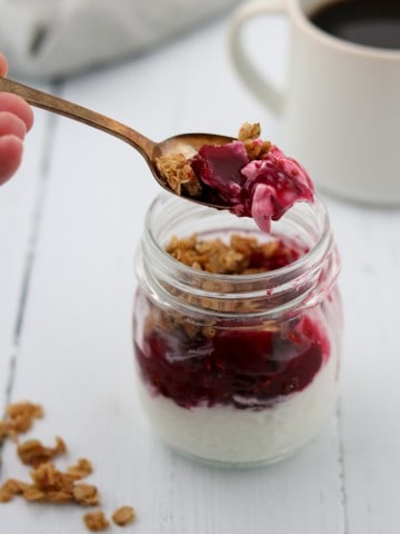 A close up of yogurt topped with raspberry, roasted beets and granola in a jar with a spoon