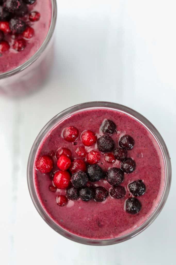 A close up of a berry smoothie topped with blueberries and lingonberries