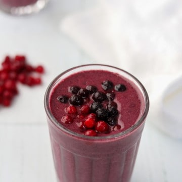 A close up of a berry smoothie topped with blueberries and lingonberries