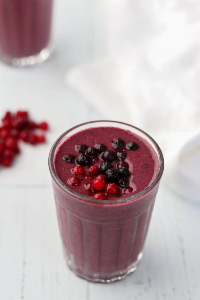 A close up of a berry smoothie topped with blueberries and lingonberries