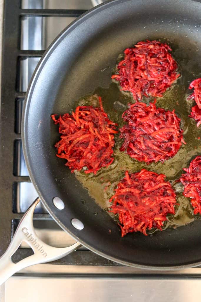 Beet and celery root cakes in a pan cooking on the stove
