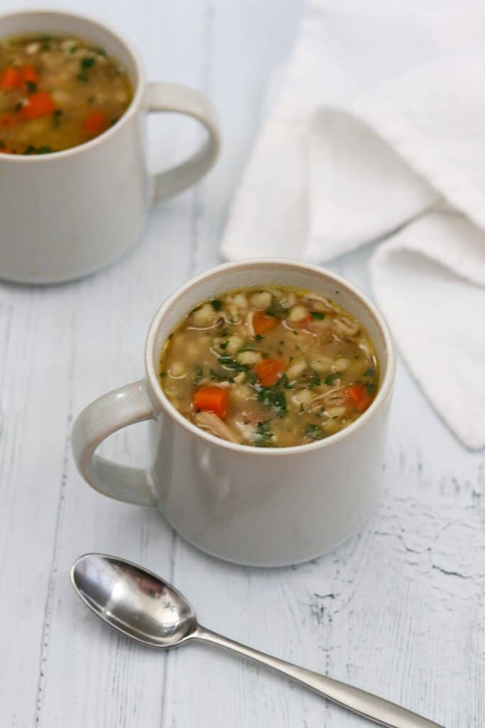 Chicken soup in a mug next to a spoon and a napkin