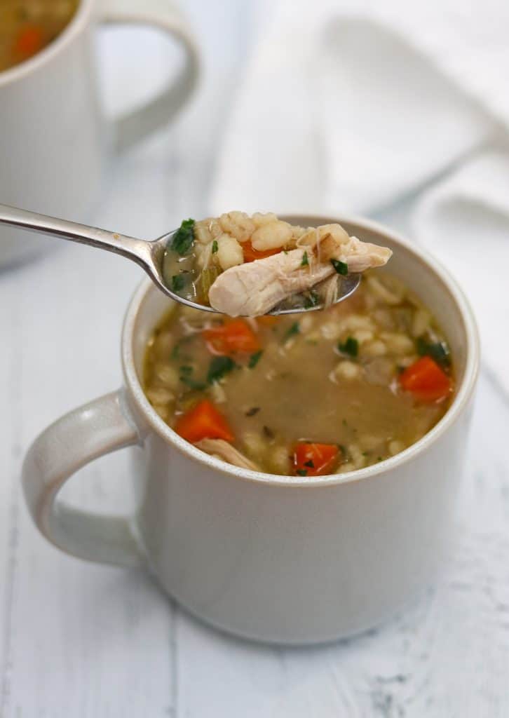 A close up of a mug of chicken soup with a spoon