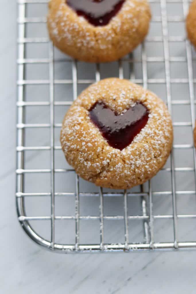 A close up of a raspberry heart cookie on a cooling rack