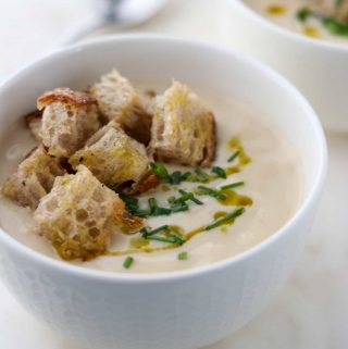 A close up of a bowl of cauliflower soup with croutons, chives and olive oil